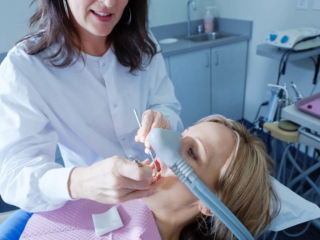 picture of woman receiving sedation in dental chair while doctor works on her teeth