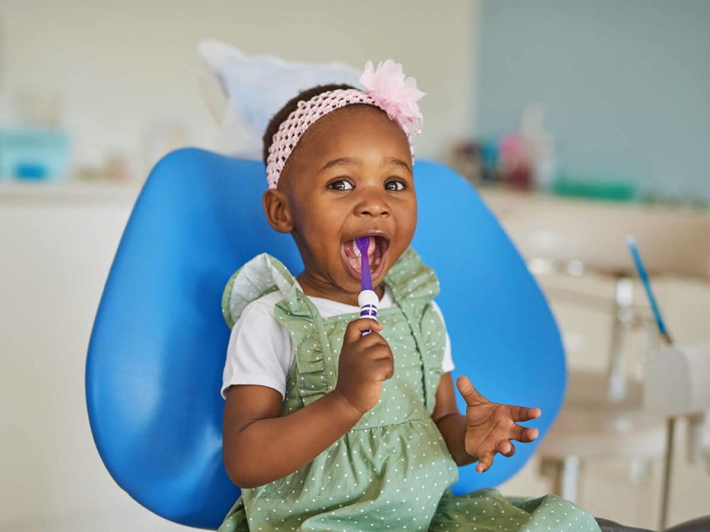 child at the dentist, holding a toothbrush in her mouth