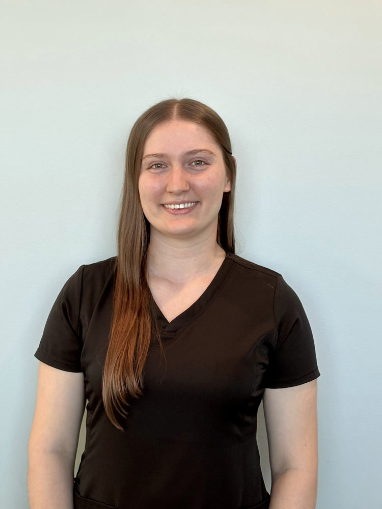 The image shows a woman wearing a black scrub top with the brand name "ARIAT" visible on the right side of the chest, against a plain light-colored background.