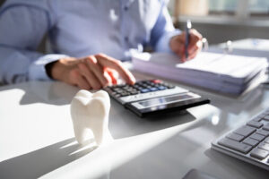 person typing on calculator with a tooth object on desk